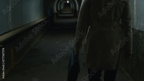 Tilt up rear view shot of man in a coat walking through the tunnel in the evening photo