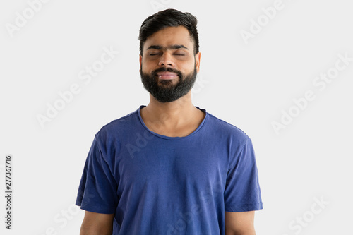 Beautiful male half-length portrait isolated on white studio background. Young emotional hindu man in blue shirt. Facial expression, human emotions, advertising concept. Standing calm with eyes closed