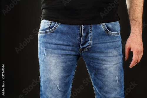 Valokuvatapetti Close up of a man in classic blue jeans trousers and black shirt against black background