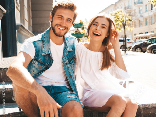 Smiling beautiful girl and her handsome boyfriend. Woman in casual summer dress and man in jeans clothes. Happy cheerful family. Sitting on stairs on the street background.Hugging couple photo
