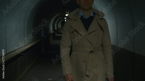 Tilt up front view shot of businessman in a coat walking through the tunnel in the evening photo