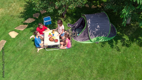 Aerial top view of family in campsite from above, parents and kids relax and have fun in park, tent and camping equipment under tree, family vacation in camp outdoors concept 