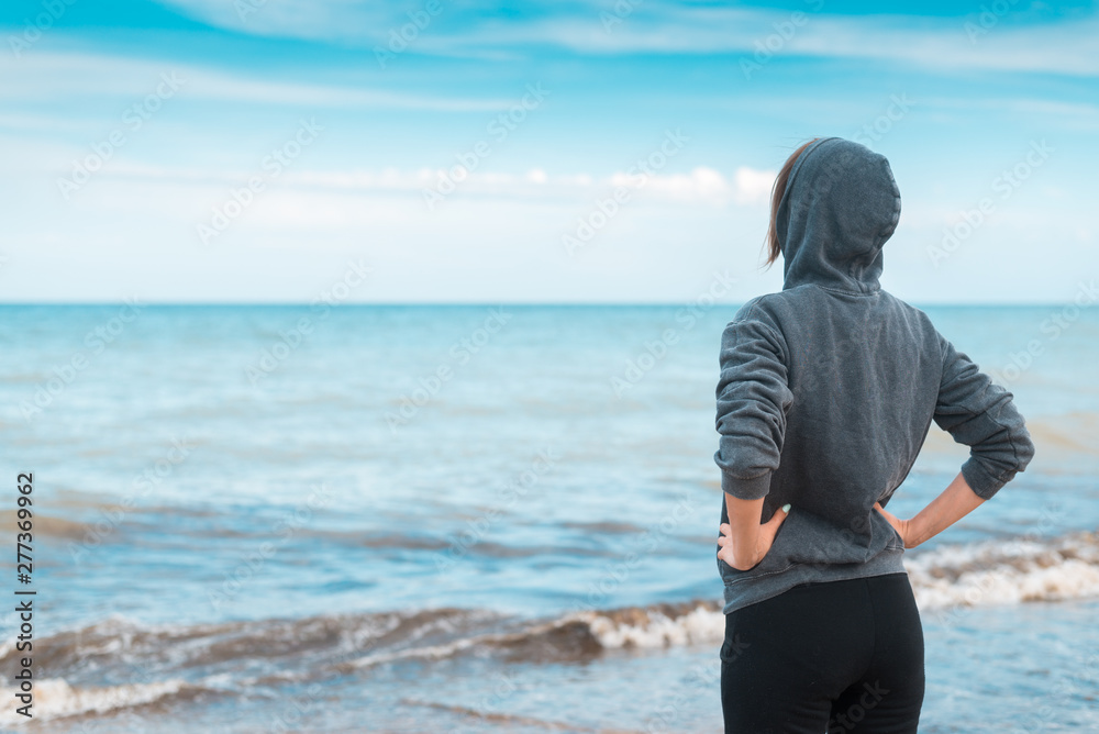 A calm, confident woman in a hooded sweater stands on the seashore, the ocean. A middle aged woman holds her hands on her belt.
