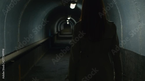 Tilt up rear view shot of redhead woman in a coat walking through the tunnel in the evening photo