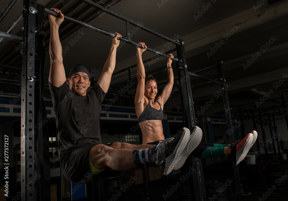 Hübsches fittes Paar hat zusammen Spaß beim Sport. Der muskulöse Mann und die athletische Frau machen im Training die Übung L sit am Reck. Sport mit dem Partner. Teamwork.  