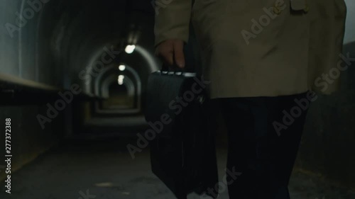 Low-section front view shot of man in a coat with case walking through the tunnel in the evening photo
