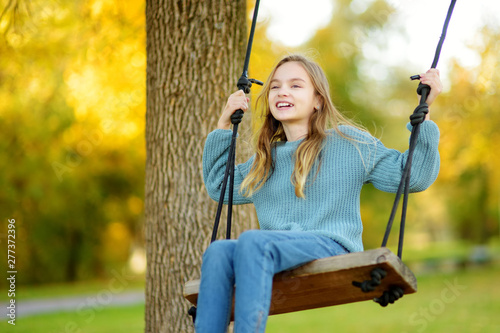 Cute young girl having fun on a swing in sunny autumn park. Family weekend in a city. photo