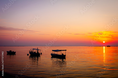 Silhouetted shot of beautiful sunrise with fisherman boats on the water