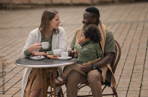happy family of three sitting in outdoors cafe and drinking coffeee