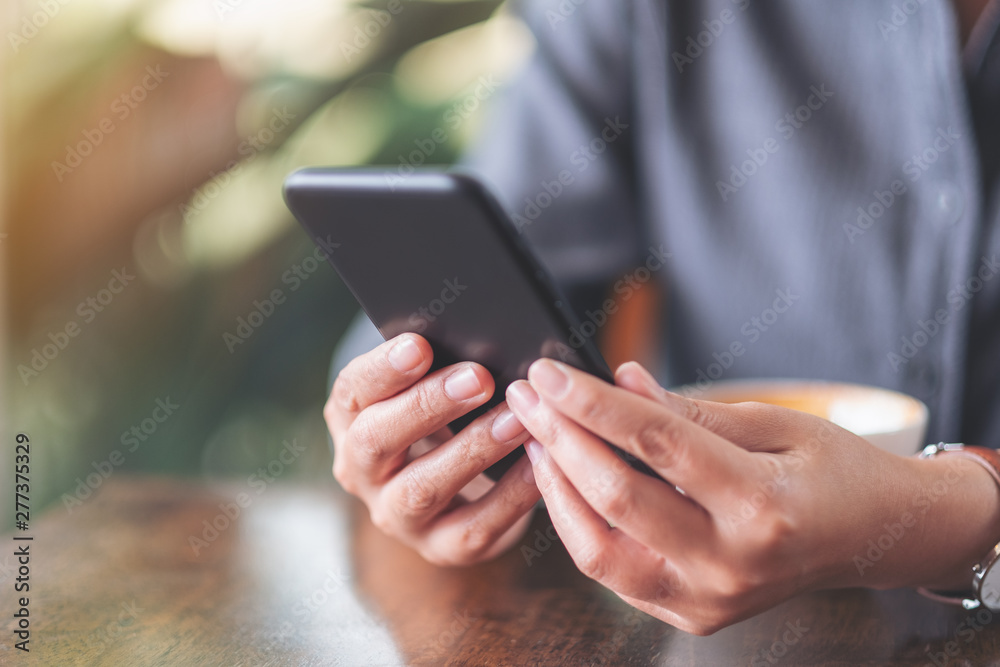 Closeup image of a woman holding  and using mobile phone with coffee cup on wooden table in cafe