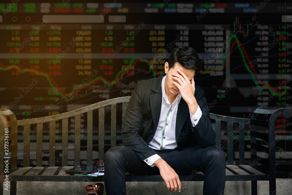 Concept of business failure and unemployment problem.An unemployed businessman sit in panic digital stock market financial background.Effect from coronavirus Concept of business failure and unemployment problem.An unemployed businessman sit in panic digital stock market financial background.Effect from coronavirus