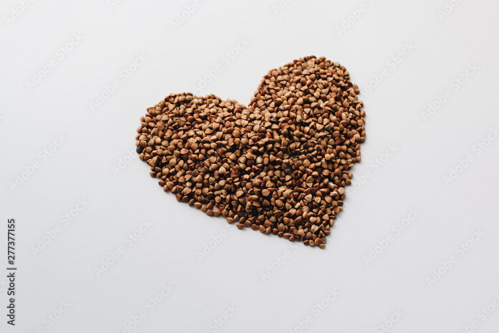 Raw buckwheat on white background shaped as heart symbol Raw buckwheat on white background shaped as heart symbol