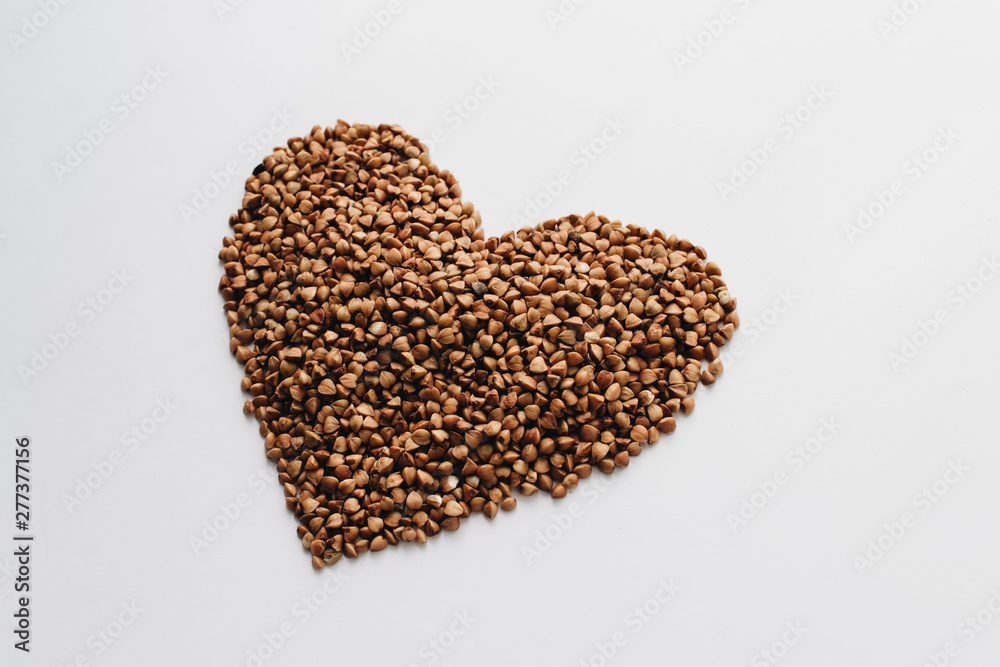 Raw buckwheat on white background shaped as heart symbol Raw buckwheat on white background shaped as heart symbol