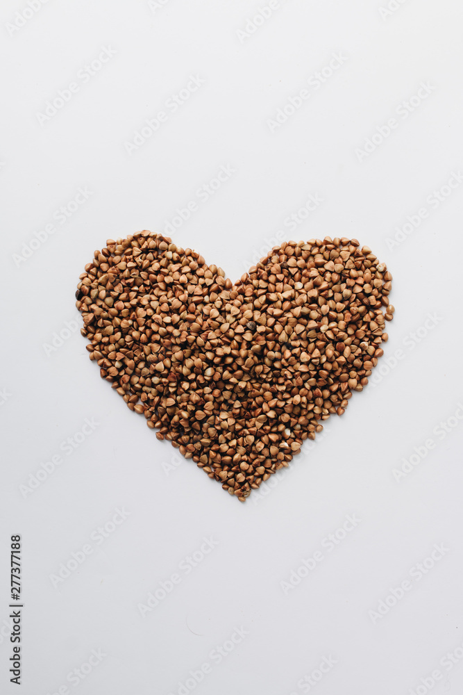 Raw buckwheat on white background shaped as heart symbol Raw buckwheat on white background shaped as heart symbol