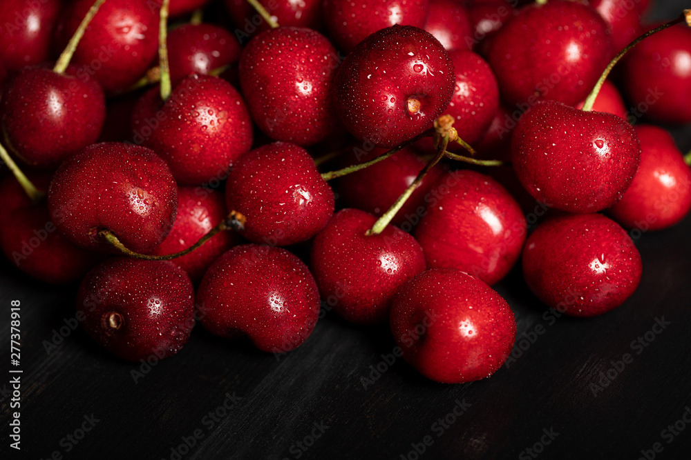 red delicious and ripe cherries with water drops on black cloth red delicious and ripe cherries with water drops on black cloth