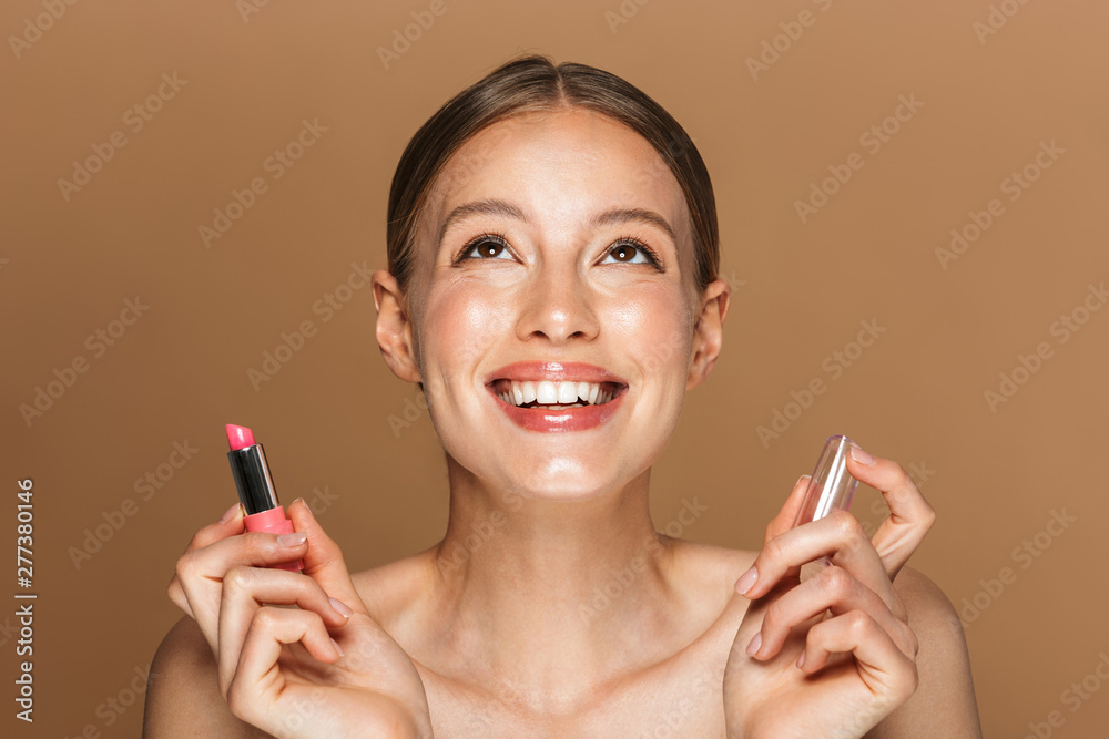 Image closeup of charming half-naked woman looking upward and holding lipstick Image closeup of charming half-naked woman looking upward and holding lipstick