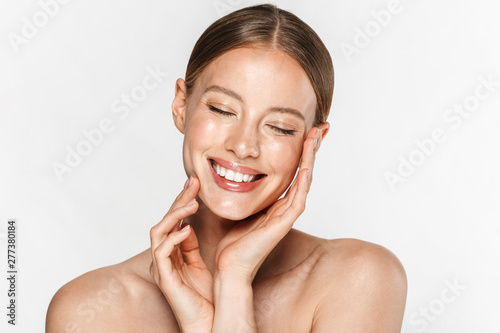 Image of adorable half-naked woman smiling at camera with eyes closed and touching her face