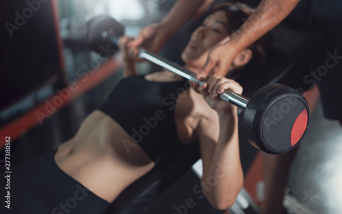 Personal trainer helping a young woman lift a barbell while working out in a gym. Personal trainer helping woman bench press in gym