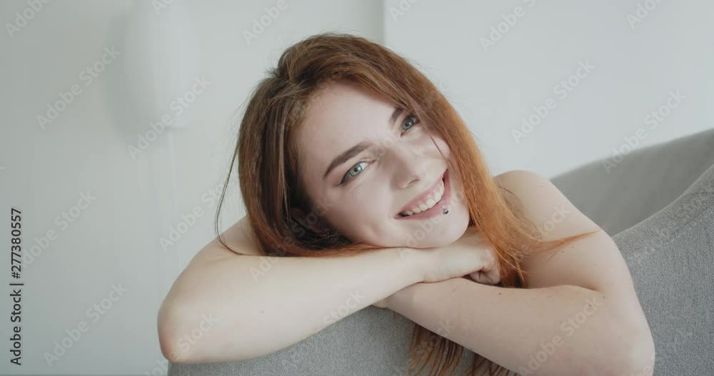 Closeup straight view shoot of young sexy caucasian female in black bodysuit laying on the couch smiling cheerfully looking at camera indoors Closeup straight view shoot of young sexy caucasian female in black bodysuit laying on the couch smiling cheerfully looking at camera indoors