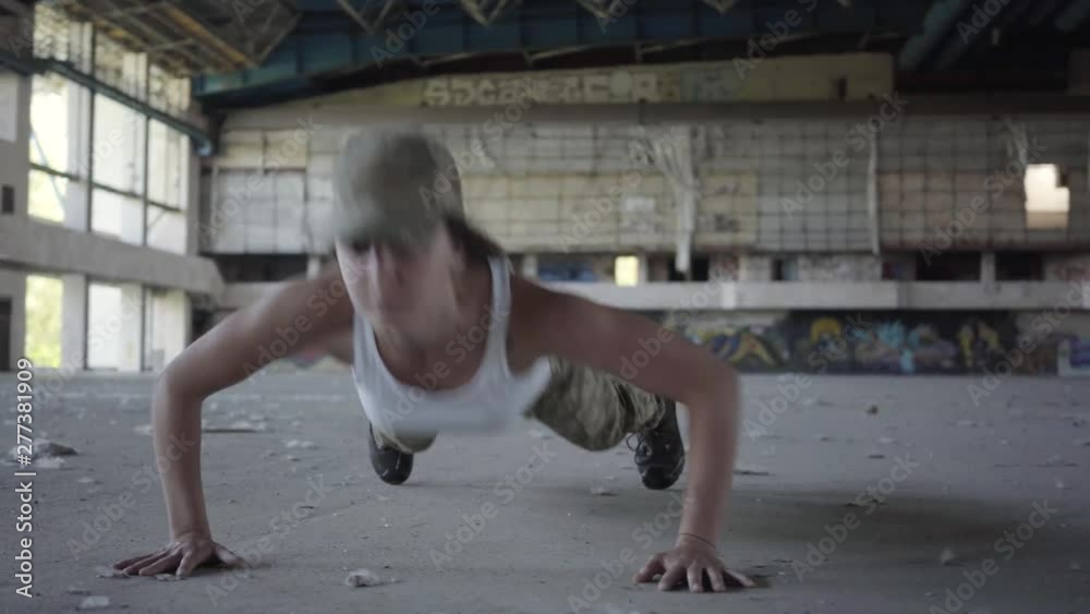Pretty strong confident young woman in military uniform push-ups in a deserted factory. High-heeled shoes lie in the foreground. Part of his cross fitness workout. High-intensity interval training. Pretty strong confident young woman in military uniform push-ups in a deserted factory. High-heeled shoes lie in the foreground. Part of his cross fitness workout. High-intensity interval training.