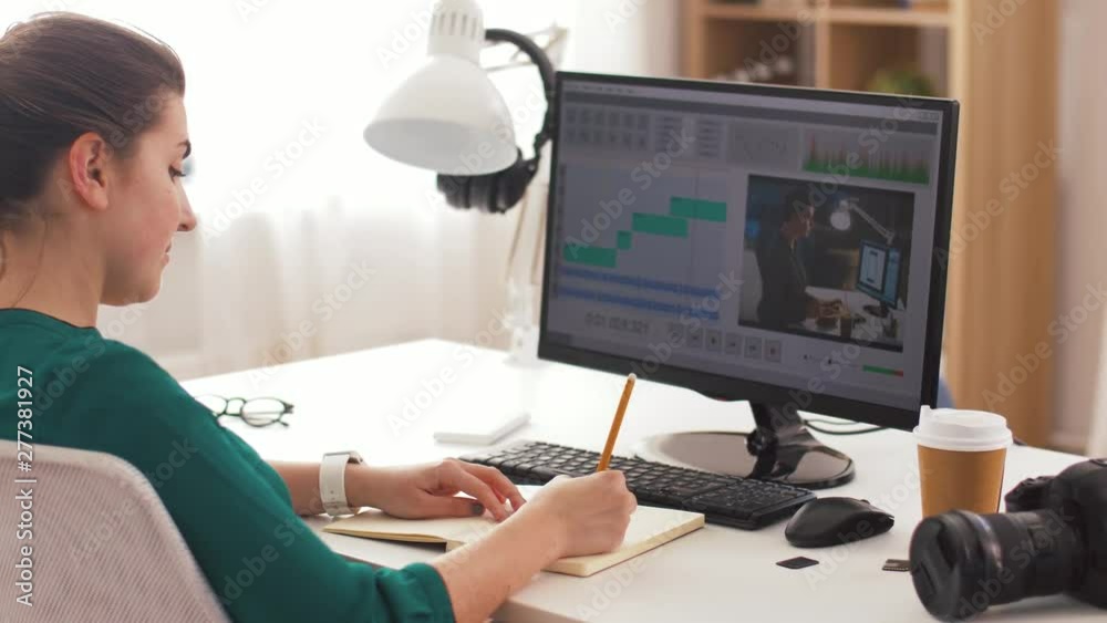 technology, post production and vlog concept - woman working in video editor program on computer writing to notebook at home office technology, post production and vlog concept - woman working in video editor program on computer writing to notebook at home office