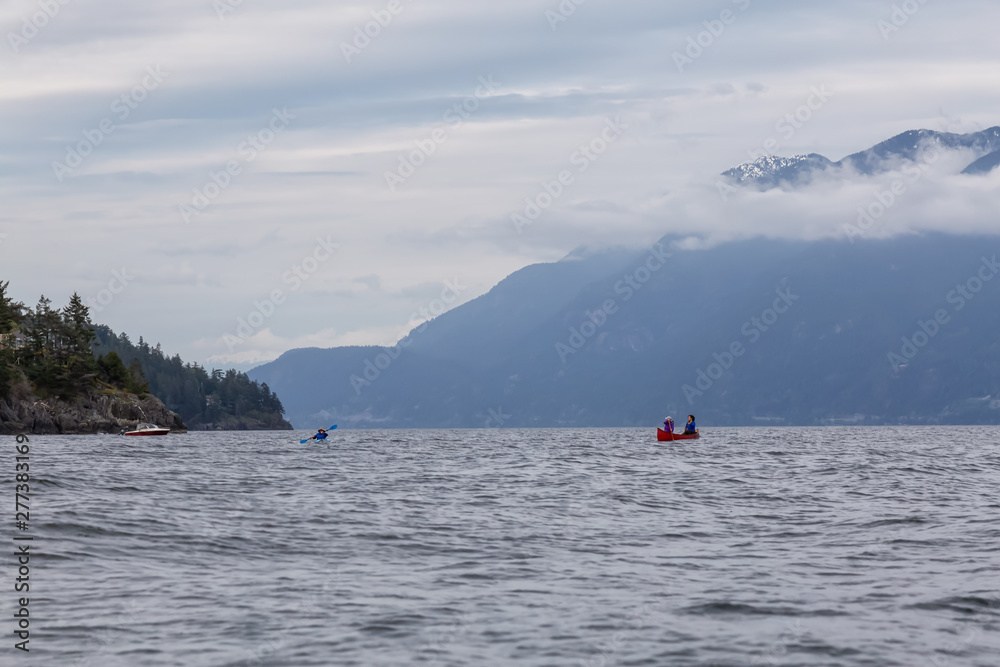 Adventurous friends on a red canoe and kayak are paddling in the Howe Sound during a cloudy sunset. Taken near Bowen Island, West of Vancouver, BC, Canada.