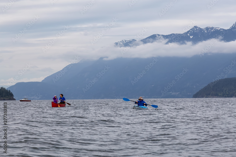 Naklejka premium Adventurous friends on a red canoe and kayak are paddling in the Howe Sound during a cloudy sunset. Taken near Bowen Island, West of Vancouver, BC, Canada.