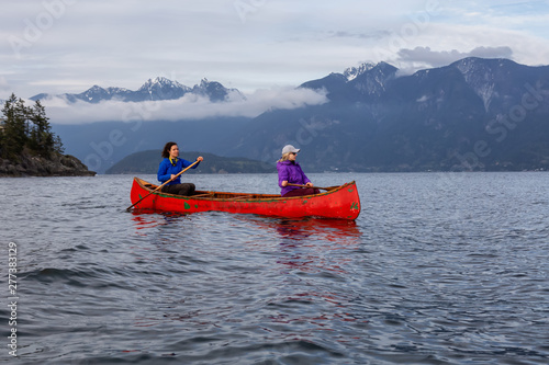 Couple adventurous female friends on a red canoe are paddling in the Howe Sound during a cloudy sunset. Taken near Bowen Island, West of Vancouver, BC, Canada. © edb3_16