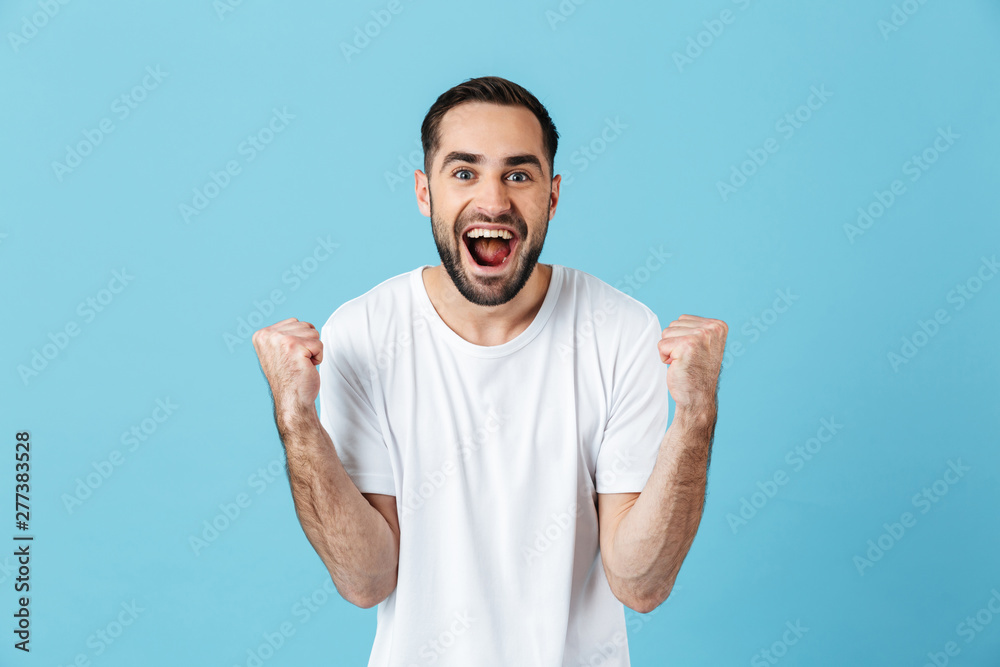 Young screaming happy bearded man posing isolated over blue wall background make winner gesture. Young screaming happy bearded man posing isolated over blue wall background make winner gesture.