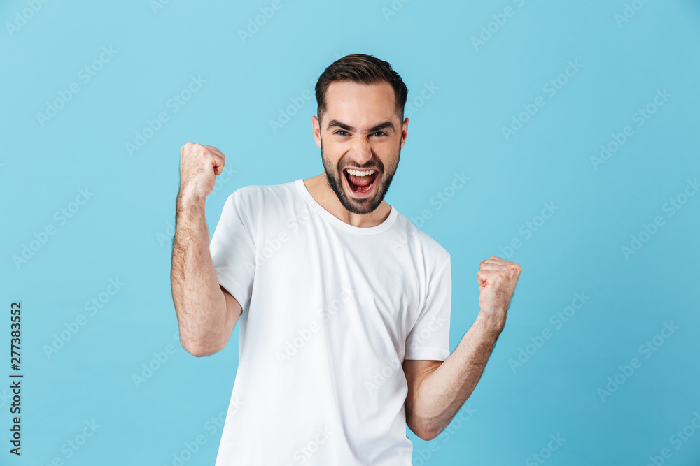Young screaming bearded man posing isolated over blue wall background make winner gesture. Young screaming bearded man posing isolated over blue wall background make winner gesture.
