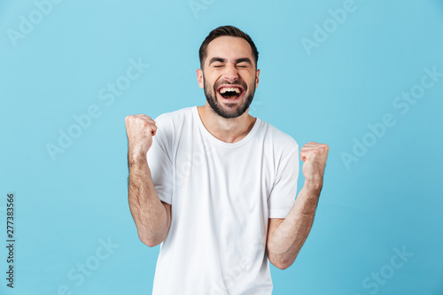 Young screaming happy bearded man posing isolated over blue wall background make winner gesture.
