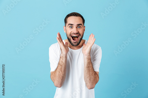 Excited young screaming happy bearded man posing isolated over blue wall background.