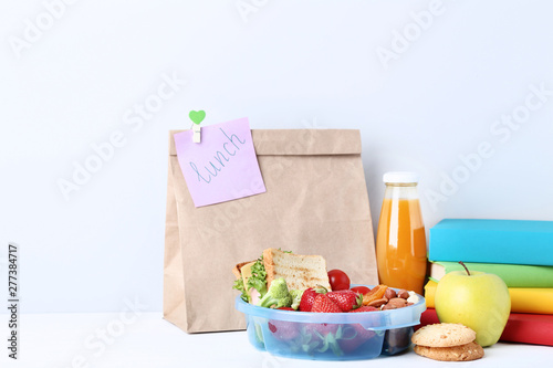 School lunch with paper bag and books on grey background