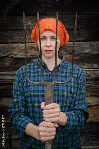 Young woman stands with a pitchfork near a stable on a ranch. photo