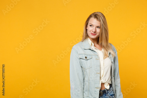Portrait of attractive smiling young woman in denim casual clothes standing and looking aside isolated on bright yellow orange wall background in studio. People lifestyle concept. Mock up copy space. © ViDi Studio
