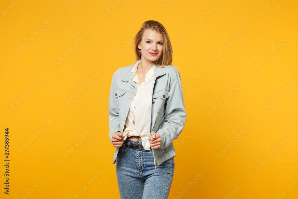 Portrait of attractive smiling young woman in denim casual clothes standing and looking camera isolated on bright yellow orange wall background in studio. People lifestyle concept. Mock up copy space. Portrait of attractive smiling young woman in denim casual clothes standing and looking camera isolated on bright yellow orange wall background in studio. People lifestyle concept. Mock up copy space.