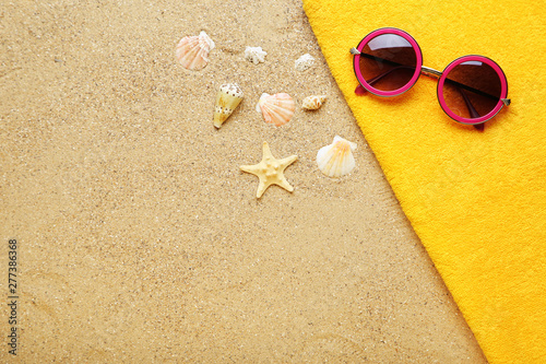 Seashells with sunglasses and towel on beach sand
