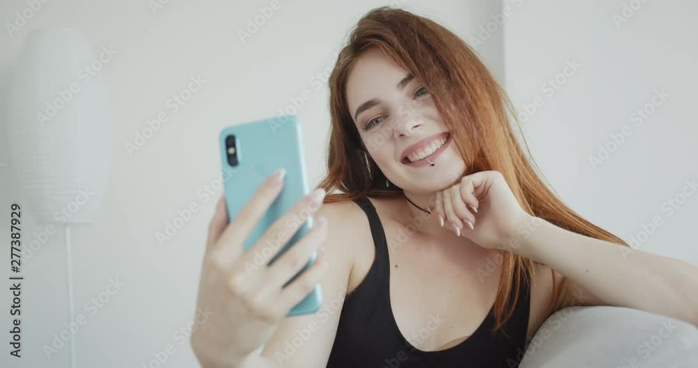 Closeup shoot of young sexy caucasian female in black bodysuit having a video call on the phone sitting on the couch indoors Closeup shoot of young sexy caucasian female in black bodysuit having a video call on the phone sitting on the couch indoors