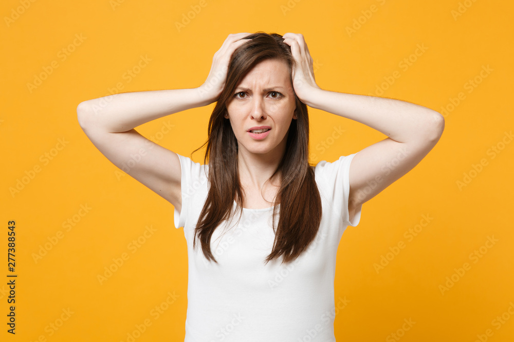Portrait of preoccupied young woman in white casual clothes looking camera, putting hands on head isolated on yellow orange wall background in studio. People lifestyle concept. Mock up copy space. Portrait of preoccupied young woman in white casual clothes looking camera, putting hands on head isolated on yellow orange wall background in studio. People lifestyle concept. Mock up copy space.