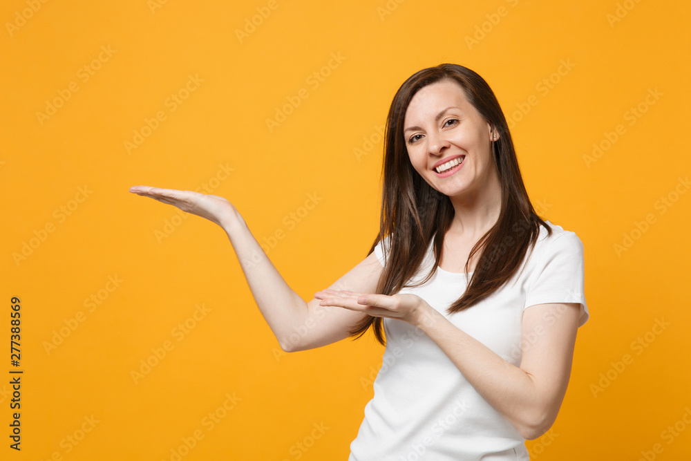 Portrait of smiling pleasant young woman in white casual clothes looking camera, pointing hands aside isolated on yellow orange wall background in studio. People lifestyle concept. Mock up copy space. Portrait of smiling pleasant young woman in white casual clothes looking camera, pointing hands aside isolated on yellow orange wall background in studio. People lifestyle concept. Mock up copy space.