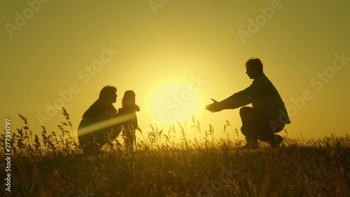 Little daughter with parents jumping at sunset. Silhouettes of mom dad and baby in the rays of dawn. Family concept. Walking with a small child in nature