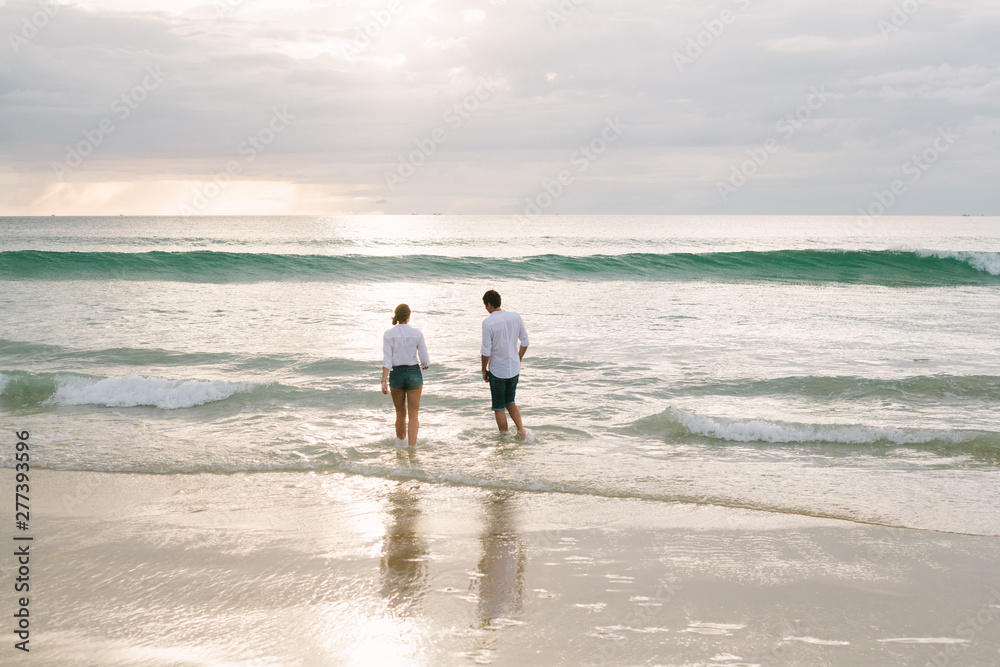 A man and a woman walk together along the seashore