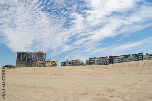 Vue de la digue depuis la plage, ciel bleu d'été avec nuages graphiques.