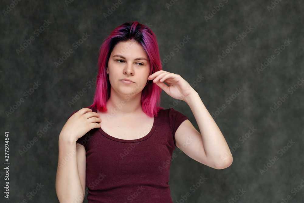 Portrait to the waist of a young pretty girl teenager in a burgundy T-shirt with beautiful purple hair on a gray background in the studio. Talking, smiling, showing hands with emotions.