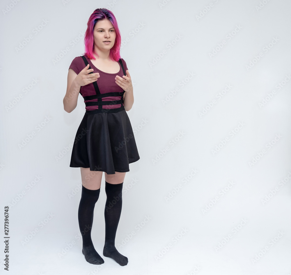 Full-length portrait of young pretty teenager girl in burgundy T-shirt and black dress with beautiful purple hair on a white background in the studio. Talking, smiling, showing hands with emotions. Full-length portrait of young pretty teenager girl in burgundy T-shirt and black dress with beautiful purple hair on a white background in the studio. Talking, smiling, showing hands with emotions.