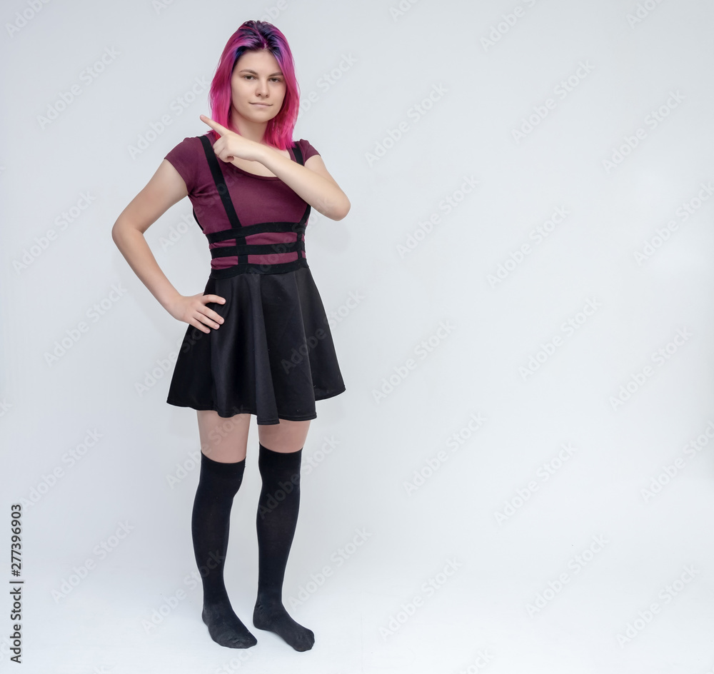 Full-length portrait of young pretty teenager girl in burgundy T-shirt and black dress with beautiful purple hair on a white background in the studio. Talking, smiling, showing hands with emotions. Full-length portrait of young pretty teenager girl in burgundy T-shirt and black dress with beautiful purple hair on a white background in the studio. Talking, smiling, showing hands with emotions.