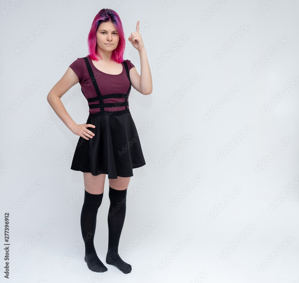 Full-length portrait of young pretty teenager girl in burgundy T-shirt and black dress with beautiful purple hair on a white background in the studio. Talking, smiling, showing hands with emotions. Full-length portrait of young pretty teenager girl in burgundy T-shirt and black dress with beautiful purple hair on a white background in the studio. Talking, smiling, showing hands with emotions.