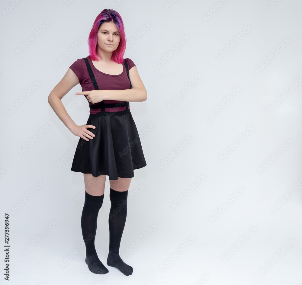 Full-length portrait of young pretty teenager girl in burgundy T-shirt and black dress with beautiful purple hair on a white background in the studio. Talking, smiling, showing hands with emotions. Full-length portrait of young pretty teenager girl in burgundy T-shirt and black dress with beautiful purple hair on a white background in the studio. Talking, smiling, showing hands with emotions.