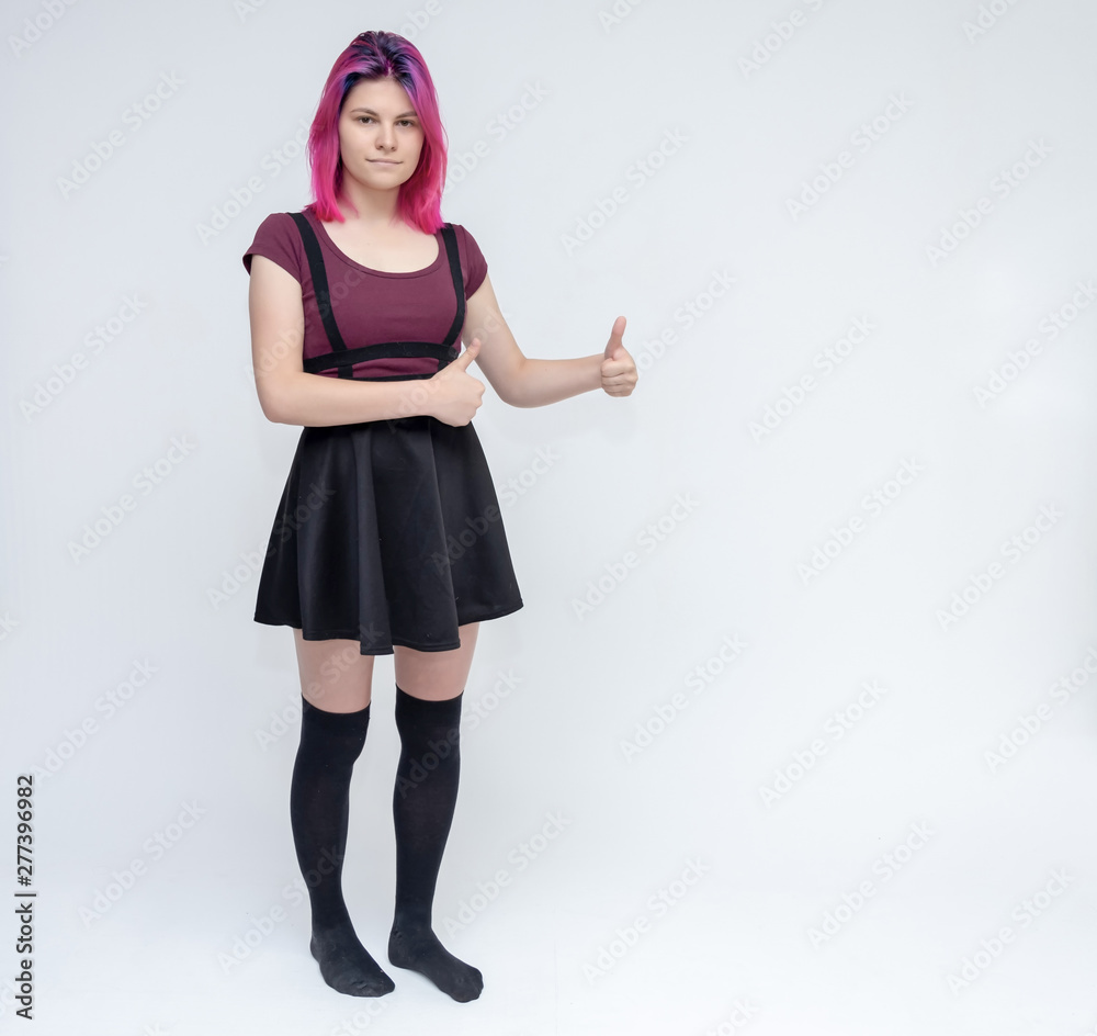 Full-length portrait of young pretty teenager girl in burgundy T-shirt and black dress with beautiful purple hair on a white background in the studio. Talking, smiling, showing hands with emotions. Full-length portrait of young pretty teenager girl in burgundy T-shirt and black dress with beautiful purple hair on a white background in the studio. Talking, smiling, showing hands with emotions.