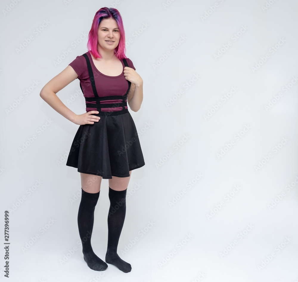 Full-length portrait of young pretty teenager girl in burgundy T-shirt and black dress with beautiful purple hair on a white background in the studio. Talking, smiling, showing hands with emotions. Full-length portrait of young pretty teenager girl in burgundy T-shirt and black dress with beautiful purple hair on a white background in the studio. Talking, smiling, showing hands with emotions.